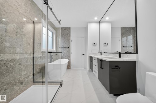 Contemporary bathroom featuring a spacious walk-in shower with stone-look tile, a freestanding bathtub, and a double vanity with dark cabinetry and black fixtures - 6117 Crawford Drive, Edmonton, AB 