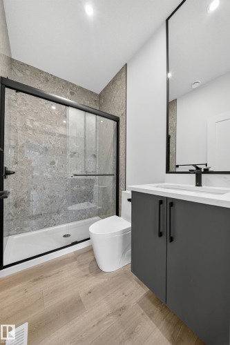 Bathroom featuring a shower with a sliding glass door, a modern toilet, and a vanity with a white countertop and dark cabinetry - 6117 Crawford Drive, Edmonton, AB 
