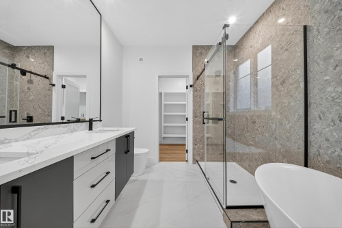 This bathroom features a contemporary double vanity with white countertops and dark cabinetry, a spacious walk-in shower with a glass enclosure, and a freestanding soaking tub - 6117 Crawford Drive, Edmonton, AB 
