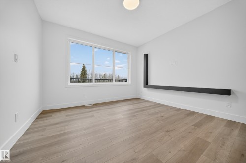 This spacious room features light-toned flooring, expansive windows providing views of trees and the sky, and a contemporary L-shaped wall fixture - 6117 Crawford Drive, Edmonton, AB 