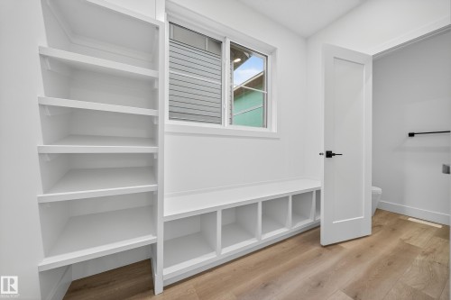 This room features built-in white shelving, a built-in white bench with cubbies, a window with horizontal blinds, and wood-style flooring - 6117 Crawford Drive, Edmonton, AB 