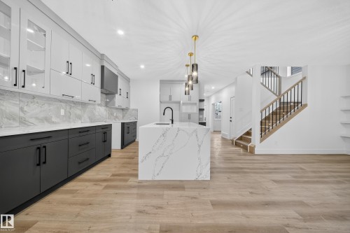 The kitchen features light-toned upper cabinetry with glass inserts, dark lower cabinetry, and a large island with a waterfall countertop - 6117 Crawford Drive, Edmonton, AB 