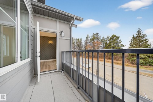 The property includes a private balcony with a dark metal railing, offering views of the surrounding trees and a road - 6117 Crawford Drive, Edmonton, AB 