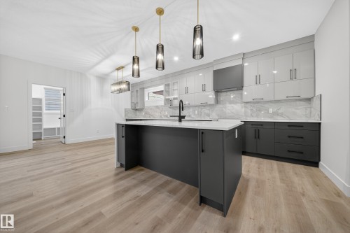 Modern kitchen featuring an island with a white countertop, dark grey cabinetry, and pendant lighting - 6117 Crawford Drive, Edmonton, AB 