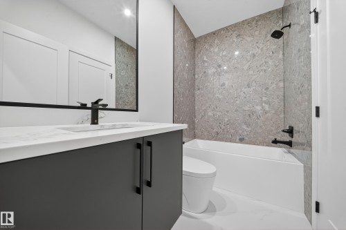 Bathroom featuring a dark gray vanity with a white countertop and a rectangular sink, a large mirror with a black frame, and a bathtub with gray tiled walls and black fixtures - 6117 Crawford Drive, Edmonton, AB 