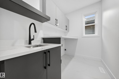 This dedicated utility area features white walls, white marbled flooring, white countertops, and dark gray cabinetry with dark hardware - 6117 Crawford Drive, Edmonton, AB 