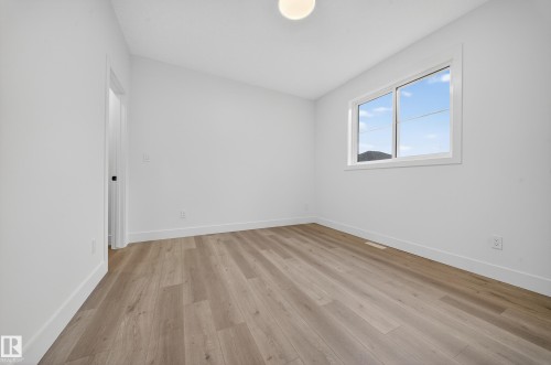 This bright room features light-colored plank flooring, white walls, and a window providing natural light and views of the outdoors - 6117 Crawford Drive, Edmonton, AB 