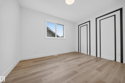 This room features light wood-look flooring, a window providing natural light, and decorative black trim accents on the wall - 6117 Crawford Drive, Edmonton, AB 