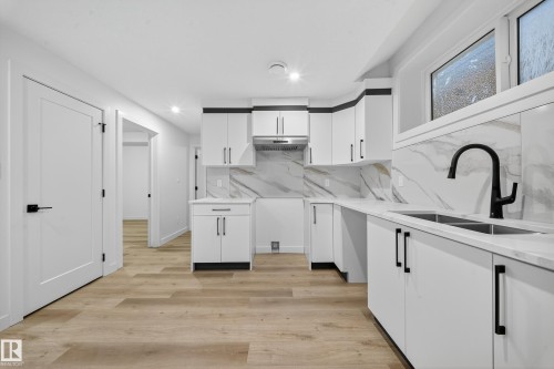 The kitchen features white cabinetry with black hardware, white countertops, and a marble-patterned backsplash - 6117 Crawford Drive, Edmonton, AB 