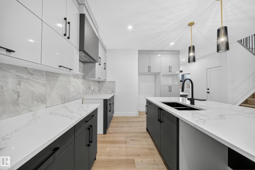 The kitchen features a contemporary design with white upper cabinetry and dark lower cabinetry, complemented by white countertops and a matching backsplash - 6117 Crawford Drive, Edmonton, AB 