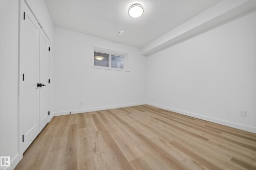 This room features light-colored plank flooring, white walls, and a window providing natural light - 6117 Crawford Drive, Edmonton, AB 