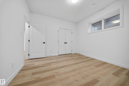 This room features light-colored plank flooring, white walls, and bright overhead lighting - 6117 Crawford Drive, Edmonton, AB 