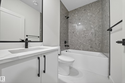 The bathroom features a modern vanity with a white countertop and dark fixtures, a bathtub with a tiled surround, and a wall-mounted mirror - 6117 Crawford Drive, Edmonton, AB 