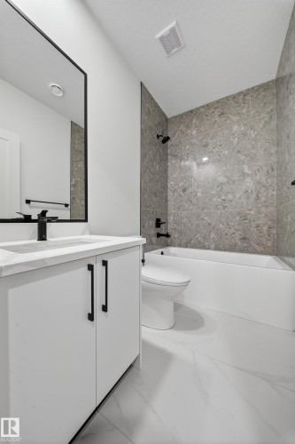 Bathroom featuring a white vanity with black hardware, a black-framed mirror, a white bathtub, and a tiled shower surround - 6117 Crawford Drive, Edmonton, AB 