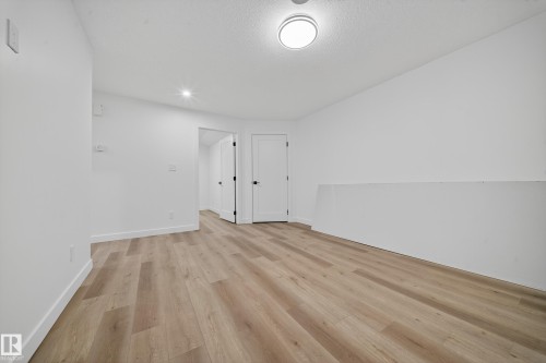 This interior space features light-toned wood-style flooring and bright white walls, creating an open and airy atmosphere - 6117 Crawford Drive, Edmonton, AB 