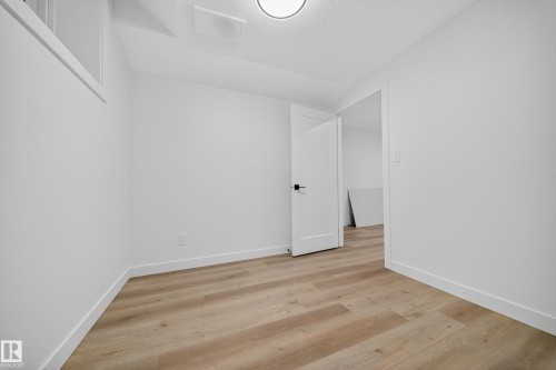 This room features light-toned wood flooring, crisp white walls, and a contemporary light fixture - 6117 Crawford Drive, Edmonton, AB 