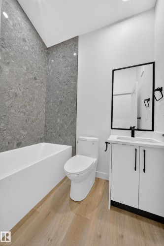 Bathroom featuring light wood-style flooring, a white bathtub with gray tiled surround, and a white vanity with a black framed mirror - 6117 Crawford Drive, Edmonton, AB 