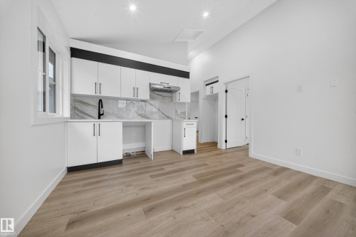 This kitchen features white cabinetry with black hardware, a contrasting black accent panel above the upper cabinets, and a white and grey veined backsplash - 6117 Crawford Drive, Edmonton, AB 