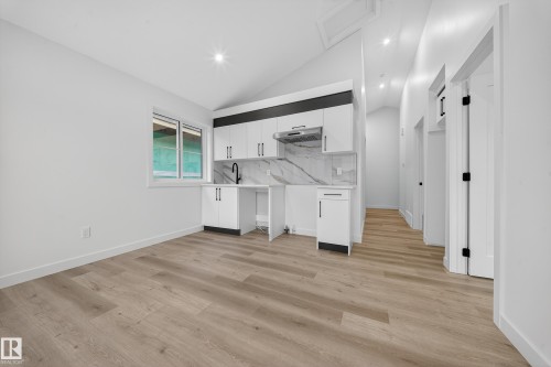 The property offers a contemporary kitchen area with white cabinetry, a stylish backsplash, and a black faucet - 6117 Crawford Drive, Edmonton, AB 