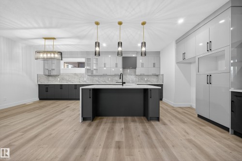 The kitchen and living area feature light-toned flooring, an island with a white countertop and dark cabinetry, and pendant lighting - 6117 Crawford Drive, Edmonton, AB 