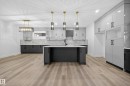 The kitchen and living area feature light-toned flooring, an island with a white countertop and dark cabinetry, and pendant lighting - 6117 Crawford Drive, Edmonton, AB 