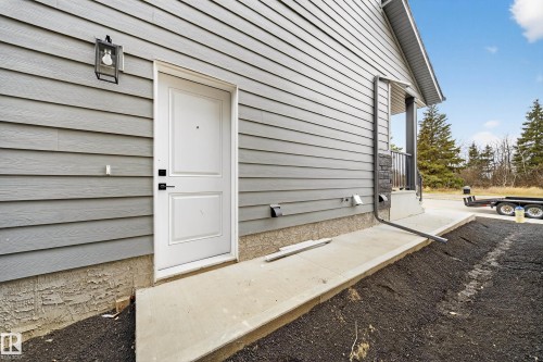 The property features gray horizontal siding and a white entry door with black hardware, complemented by a black exterior light fixture - 6117 Crawford Drive, Edmonton, AB 