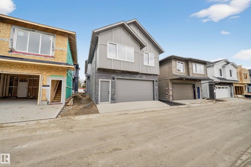 The property features a contemporary exterior with grey siding and stone accents, a private entry door, and an attached two-car garage - 6117 Crawford Drive, Edmonton, AB 