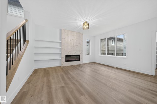 This bright living area features light wood-look flooring, a modern fireplace with a light-colored marble-look surround, and built-in shelving - 6117 Crawford Drive, Edmonton, AB 