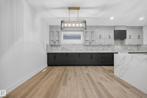 The kitchen features a contemporary design with two-tone cabinetry, a marbled backsplash, and a spacious island with a striking veined countertop - 6117 Crawford Drive, Edmonton, AB 