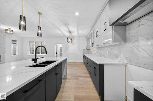 The kitchen features a large island with a double sink and a modern black faucet, complemented by white countertops with gray veining - 6117 Crawford Drive, Edmonton, AB 
