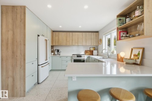 The kitchen features light wood tone and light blue cabinets, a white refrigerator, a stainless steel range, and light countertops - 7235 112 Street, Edmonton, AB - Indoor Photo Showing Kitchen