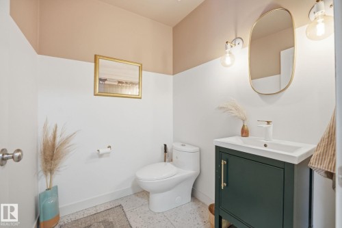 The bathroom features a modern vanity with a white basin and dark green cabinetry, a wall-mounted mirror, and stylish sconce lighting - 7235 112 Street, Edmonton, AB - Indoor Photo Showing Bathroom
