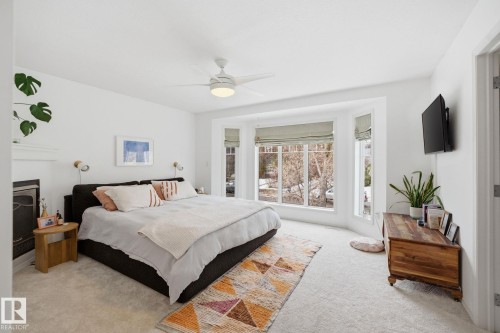 This room features light-colored carpeting, a fireplace with a white mantel, and a bay window providing exterior views - 7235 112 Street, Edmonton, AB - Indoor Photo Showing Bedroom