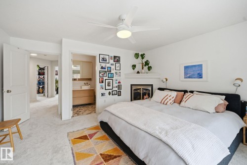 This bedroom features a ceiling fan with integrated lighting, a fireplace, and light-colored carpeting - 7235 112 Street, Edmonton, AB - Indoor Photo Showing Bedroom