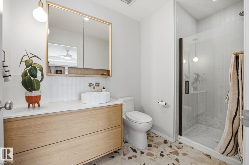 The bathroom features a floating wooden vanity with a white countertop and a vessel sink, a mirrored medicine cabinet, and a glass-enclosed shower with a dark frame - 7235 112 Street, Edmonton, AB - Indoor Photo Showing Bathroom