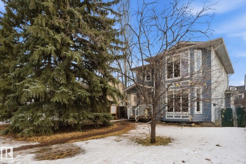 The property features a two-story exterior with light blue siding and white trim, complemented by a large evergreen tree - 7235 112 Street, Edmonton, AB - Outdoor