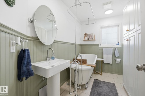 This bathroom features a pedestal sink with a chrome faucet, a freestanding clawfoot tub with a shower curtain rod, and a window with frosted glass - 7235 112 Street, Edmonton, AB - Indoor Photo Showing Bathroom