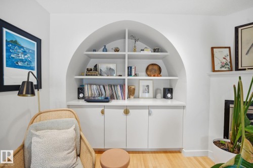 This room features built-in white cabinetry with gold-toned hardware, an arched recessed shelving unit, and warm-toned hardwood flooring - 7235 112 Street, Edmonton, AB - Indoor