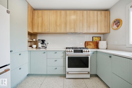 The kitchen features light wood upper cabinetry and light blue lower cabinetry, complemented by a white countertop and a white range - 7235 112 Street, Edmonton, AB - Indoor Photo Showing Kitchen