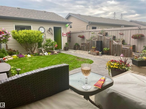 The property features a well-maintained yard with a lush lawn, a paved pathway, and various planted flowers and shrubs - 2914 18A Avenue, Edmonton, AB - Outdoor With Deck Patio Veranda