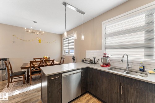 The kitchen features dark wood cabinetry, a double basin stainless steel sink, and light countertops, complemented by a white subway tile backsplash - 79 17635 58 Street, Edmonton, AB - Indoor Photo Showing Kitchen With Double Sink