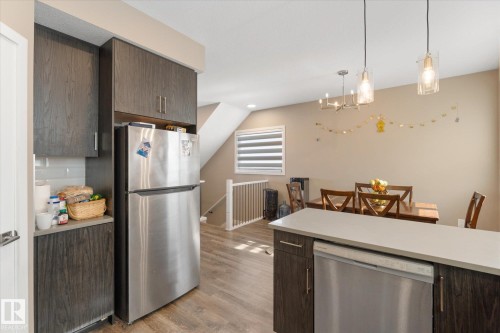The property features an open kitchen and dining area with dark wood cabinetry, a stainless steel refrigerator, and a dishwasher - 79 17635 58 Street, Edmonton, AB - Indoor Photo Showing Kitchen