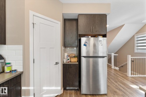 The kitchen features wood-look flooring, dark wood cabinetry, a stainless steel refrigerator, and white subway tile backsplash - 79 17635 58 Street, Edmonton, AB - Indoor Photo Showing Kitchen