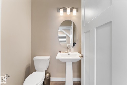 The bathroom features a white pedestal sink with a chrome faucet, a white toilet, and an oval mirror - 79 17635 58 Street, Edmonton, AB - Indoor Photo Showing Bathroom
