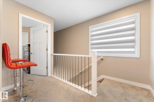 This area features light-colored walls and carpeting, a window with blinds, and a white banister with metal spindles - 79 17635 58 Street, Edmonton, AB - Indoor Photo Showing Other Room