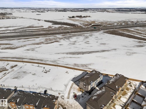 Aerial view showcasing residential properties with dark-colored roofs and light-colored siding, situated near a multi-lane highway - 79 17635 58 Street, Edmonton, AB - Outdoor With View