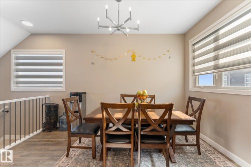 Dining area featuring a modern chandelier, two windows with blinds, and light-colored walls - 79 17635 58 Street, Edmonton, AB - Indoor Photo Showing Dining Room