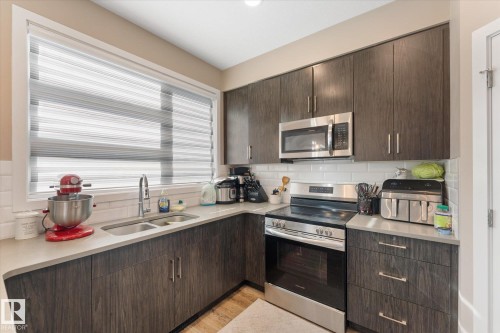 The property features a kitchen with dark wood cabinetry, a double basin sink, and a stainless steel oven with a microwave above - 79 17635 58 Street, Edmonton, AB - Indoor Photo Showing Kitchen With Double Sink