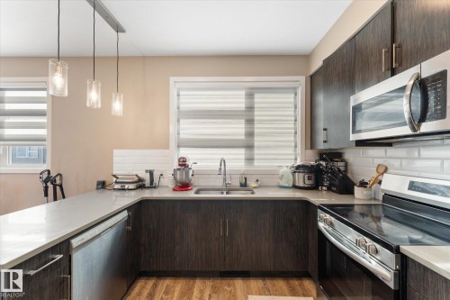 The kitchen features dark wood cabinetry, stainless steel appliances, a white subway tile backsplash, and light-colored countertops - 79 17635 58 Street, Edmonton, AB - Indoor Photo Showing Kitchen With Double Sink