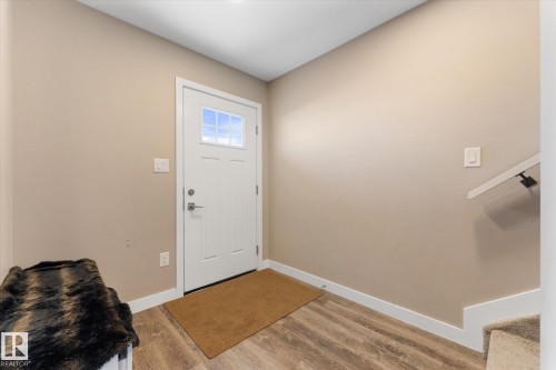 The property features neutral-toned walls, wood-style flooring, a white front door with window panelling, and a white handrail - 79 17635 58 Street, Edmonton, AB - Indoor Photo Showing Other Room